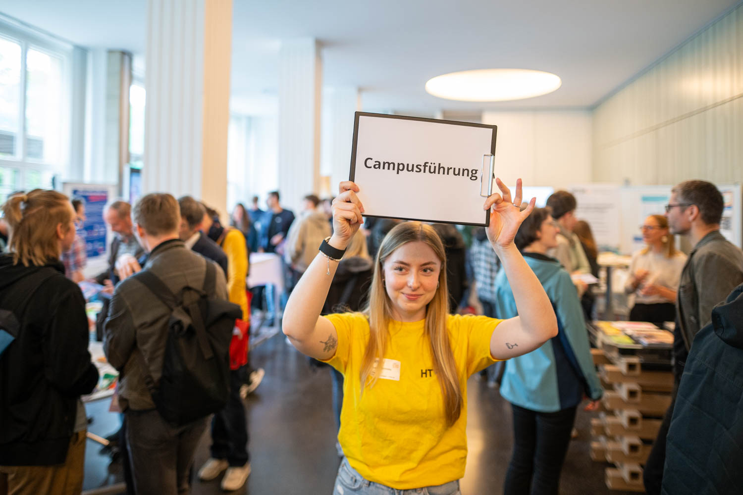 Junge Frau im PAB hält Schild mit Aufschrift Campusführung hoch