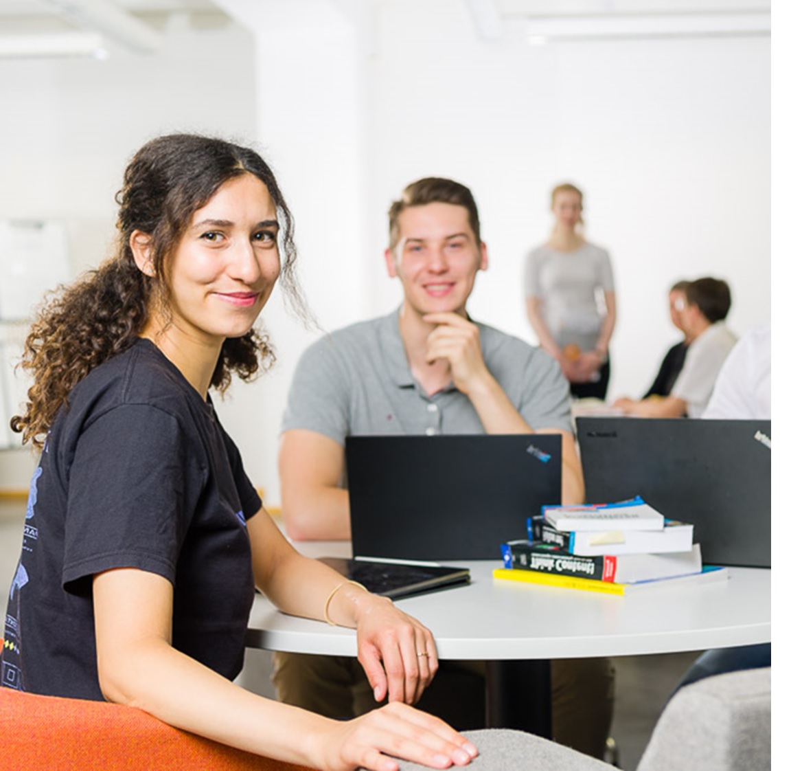 eine weibliche Studierende und ein männlicher Student sitzen an einem Tisch und lächeln in die Kamera