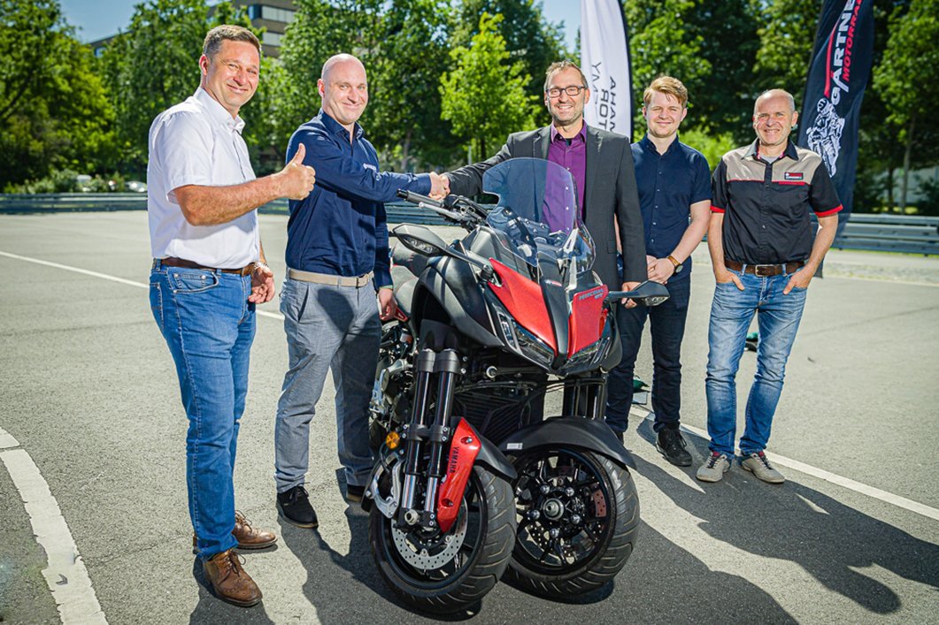 fünf Männer stehen neben einem dreirädrigem Motorrad