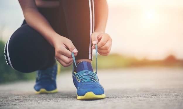 Nahaufnahme einer knieenden Person, die sich die Laufschuhe zubindet