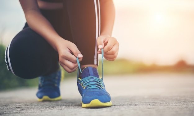 Nahaufnahme einer knieenden Person, die sich die Laufschuhe zubindet