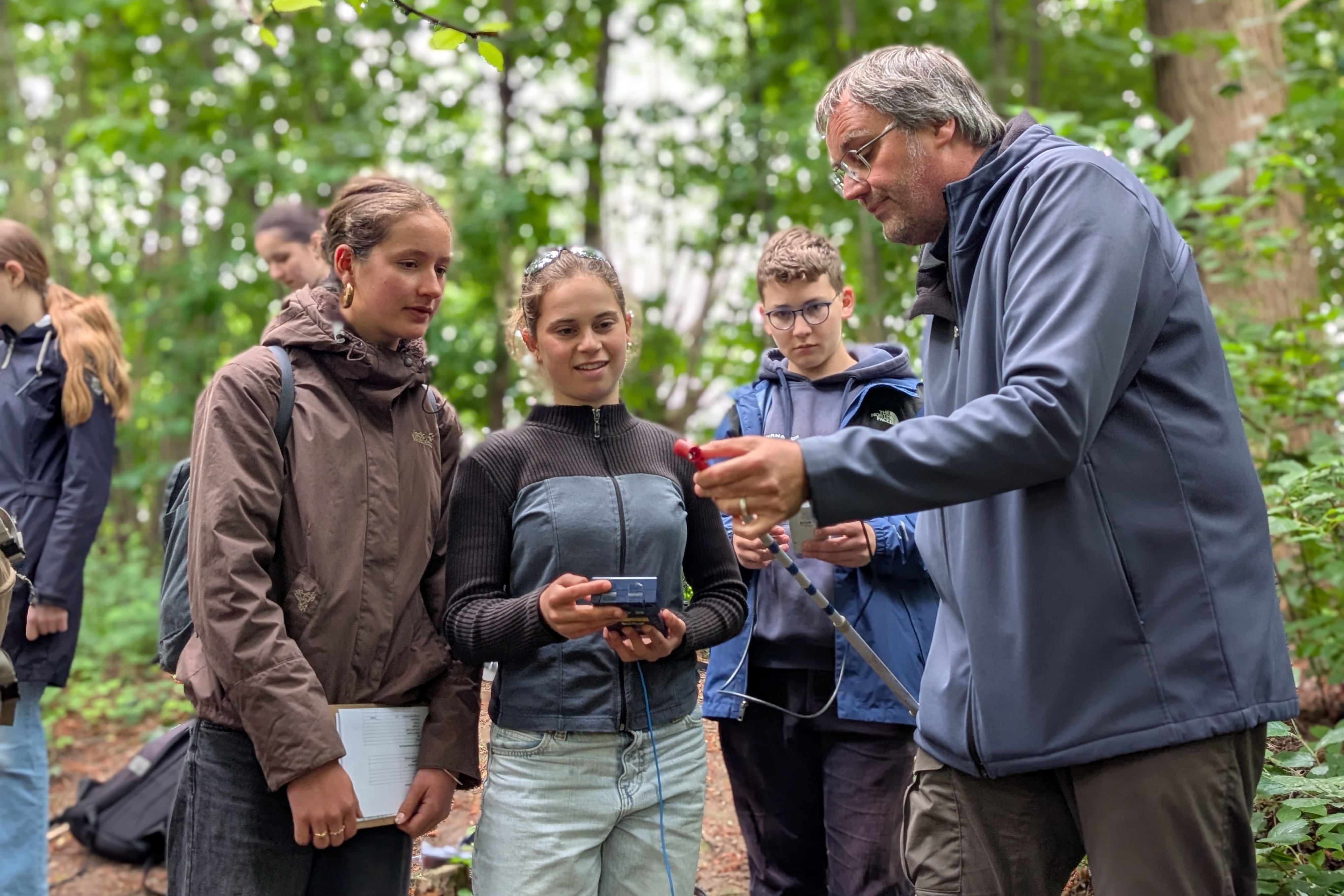 Schüler stehen mit Messgeräten neben einem Forscher im Wald