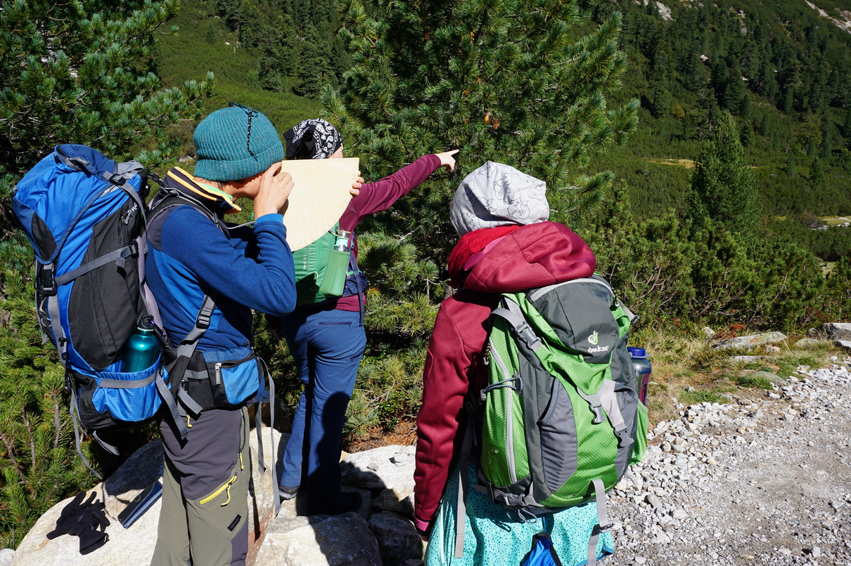 3 Personen mit Wanderausrüstung auf einem Wanderweg, Bäume im Hintergrund