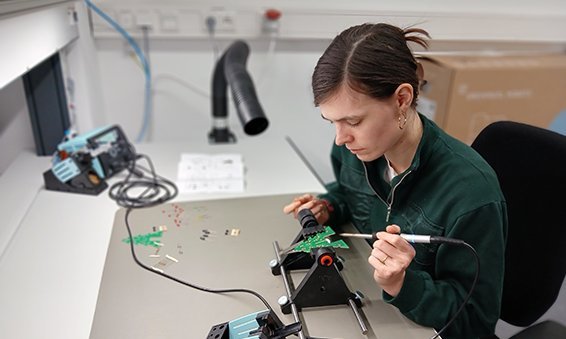 Eine Frau sitz an einem Elektronikarbeitsplatz und lötet Bauteile zusammen